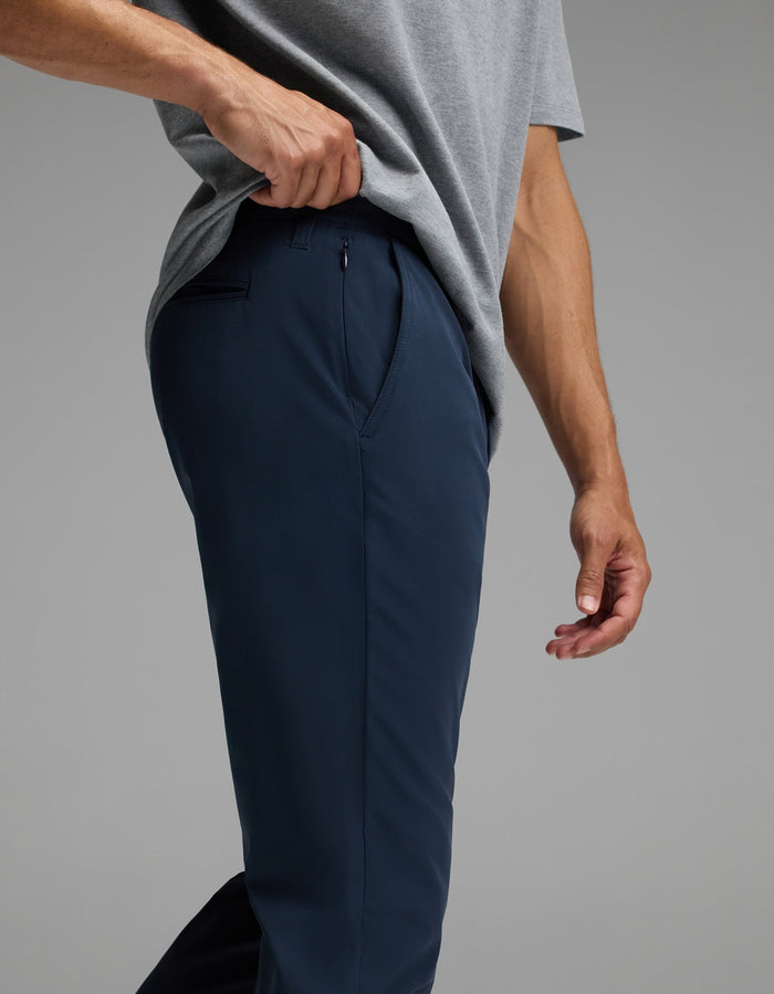 A person wearing a grey shirt and navy blue Cozy Earth Men’s Everywhere Pant stands with one hand lifting the shirt slightly, revealing the waistband and top of the pants.|Color:Eclipse