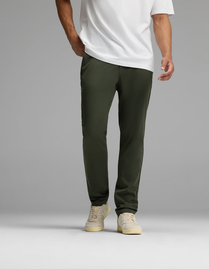 A person wearing Cozy Earth’s Men’s Everywhere Pant in olive green is pictured standing against a plain gray background. The image is cropped at the shoulders, focusing on the lower torso and legs.|Color:Olive