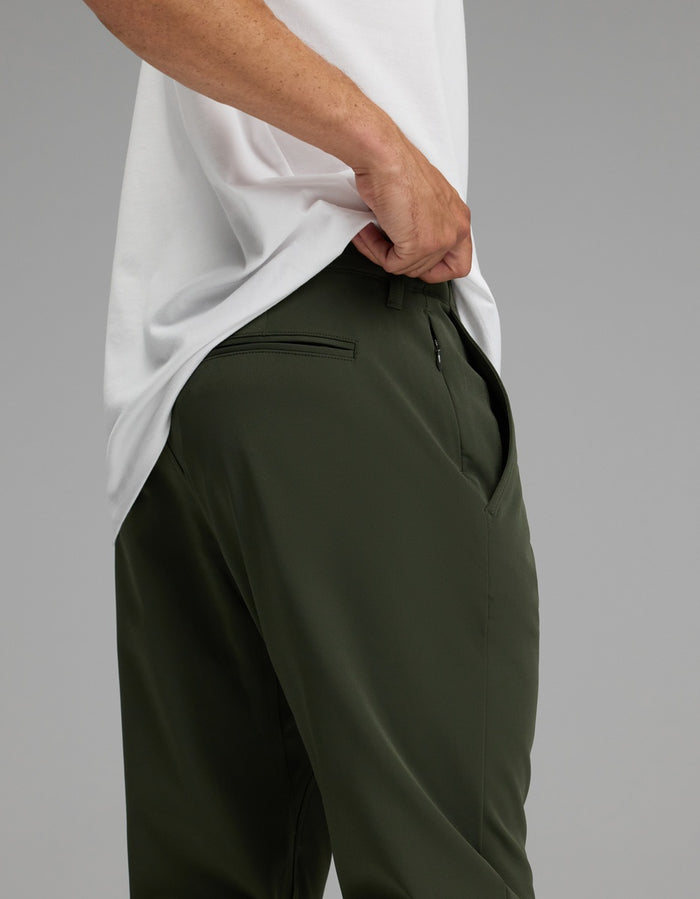 A person wearing Cozy Earth’s Men’s Everywhere Pant in dark green stands with one hand in their pocket against a plain background.|Color:Olive