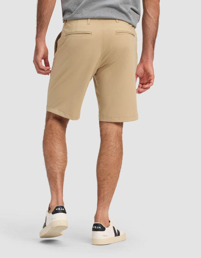 A man stands with his back to the camera against a plain light background, wearing Cozy Earth Men's Everywhere Short in tan, a gray shirt, and white Veja sneakers.|Color:Sandalwood