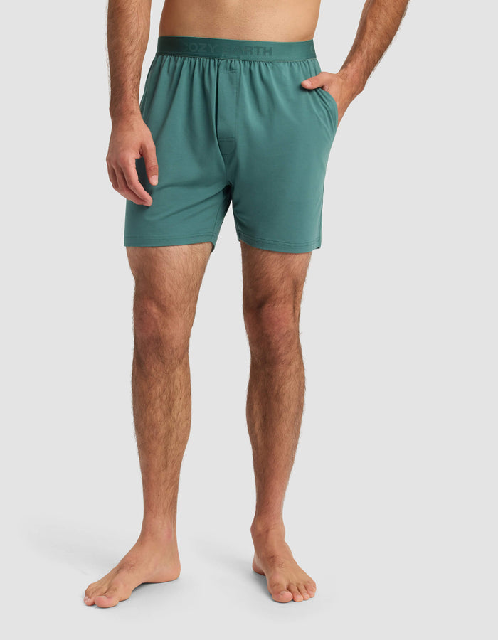 A man stands barefoot in Cozy Earth Men's First Layer Pajama Shorts with an elastic waistband, one hand in his pocket, against a plain light gray background.|Color:Sea Green