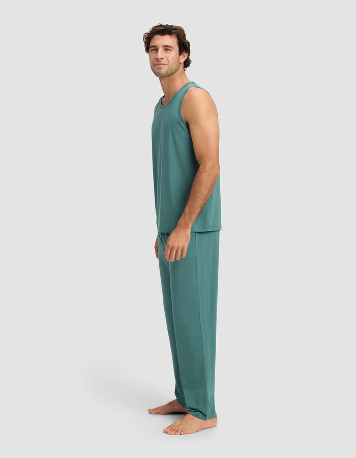 A man stands barefoot on a plain background, wearing the Cozy Earth Men's First Layer Pajama Tank & Pant Set in teal, looking at the camera with a relaxed expression.|Color:Sea Green