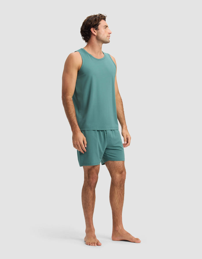 A man stands barefoot in the Cozy Earth Men's First Layer Pajama Tank & Short Set, facing slightly to the side against a plain, light background.|Color:Sea Green