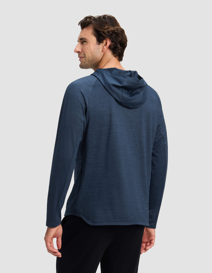 A man with short brown hair is seen from behind wearing Cozy Earth’s Men’s Lightweight Performance Hoodie in dark blue and black pants, standing against a plain light gray background.|Color:Heather Eclipse