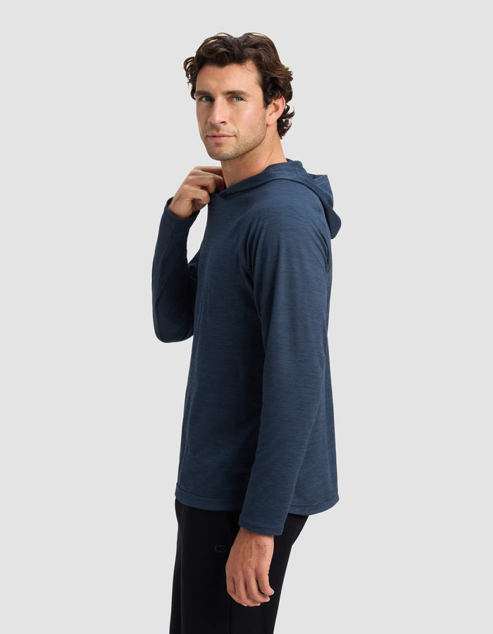 A man in a Cozy Earth Men's Lightweight Performance Hoodie stands sideways against a plain light grey background, turning his head to the camera and touching his collar, wearing black pants.|Color:Heather Eclipse