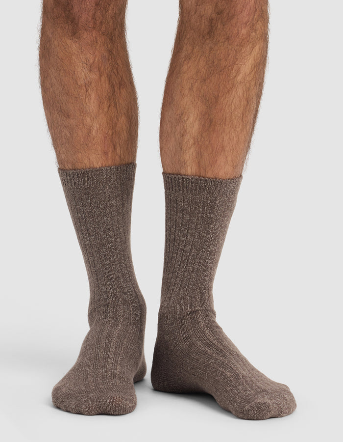 A close-up of a person's lower legs and feet wearing Cozy Earth’s The Plush Lounge Calf Sock 3-Pack in brown, ribbed, crew-length style, set against a plain white background.|Color:Cacao/Taupe/Alabaster