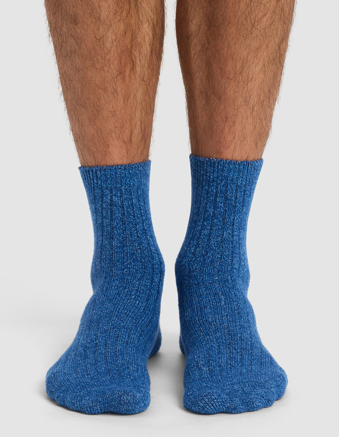 A pair of feet wearing Cozy Earth's Plush Lounge Quarter Socks from the 3-Pack, in blue. The socks are thick and ribbed, and the wearer stands on a white surface with their lower legs showing.|Color:Pacific/Harbor/Lake