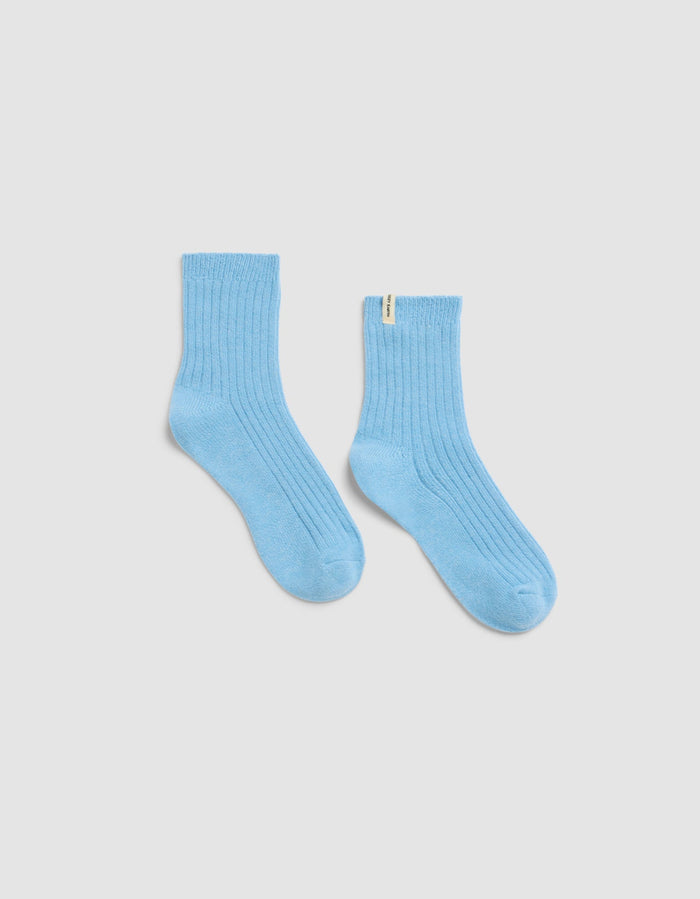 The Plush Lounge Quarter Sock by Cozy Earth in light blue features a ribbed design and a small yellow tag on the upper edge, shown against a plain white background.|Color:Harbor
