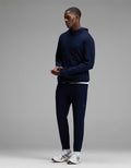 A man stands wearing the Cozy Earth Men’s Recovery Jogger in navy, paired with a matching navy hooded sweatshirt and white athletic sneakers, set against a plain gray background.|Color:Navy