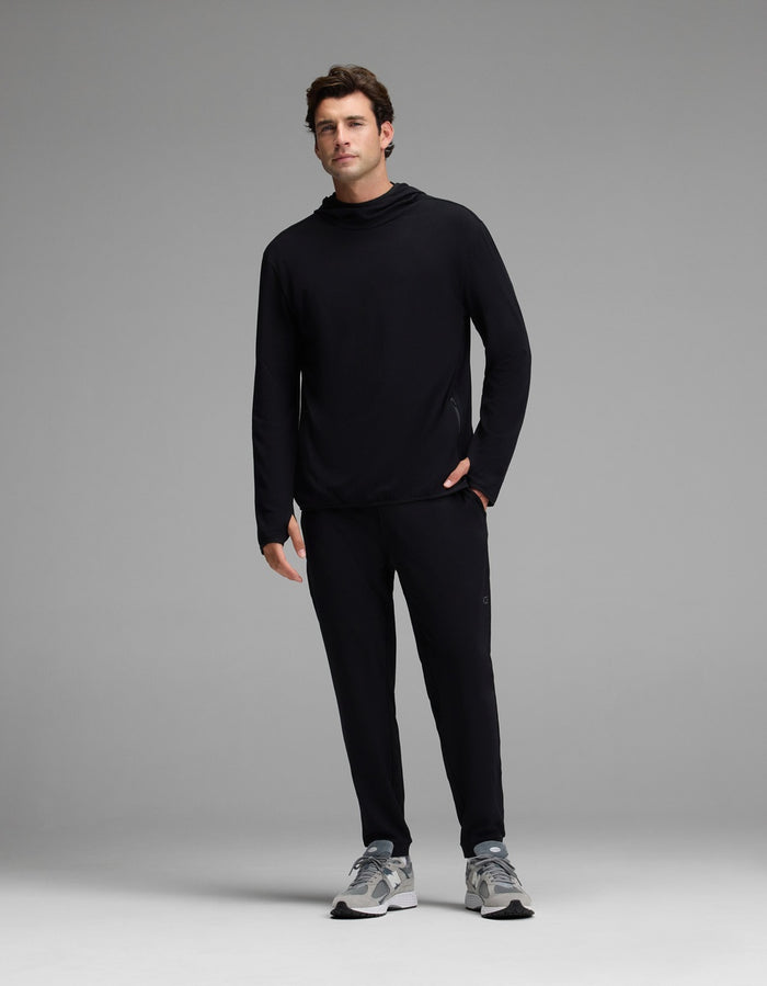 A man stands facing forward wearing Cozy Earth’s Men’s Recovery Jogger in black, paired with a black long-sleeve shirt and gray sneakers against a plain light gray background.|Color:Black