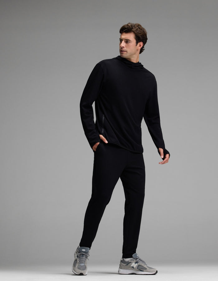 A man is seen wearing the Cozy Earth Men’s Recovery Hoodie & Jogger Set in black, paired with gray sneakers, as he stands against a plain gray background and looks to his left.|Color:Black
