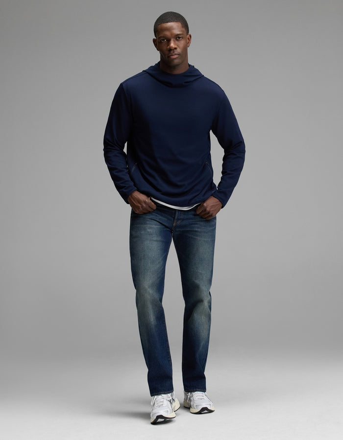 A man stands facing forward against a plain grey background, wearing the Cozy Earth Men’s Recovery Hoodie in navy, blue jeans, and white sneakers.|Color:Navy
