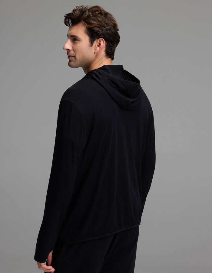 A man with short brown hair is standing and looking to his left, with his back and left side visible against a plain gray background. He is wearing the Cozy Earth Men’s Recovery Hoodie in black.|Color:Black