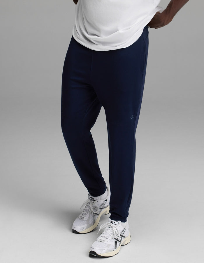 A person wearing a white shirt, Cozy Earth Men’s Recovery Jogger in navy, and white athletic sneakers stands against a plain gray background.|Color:Navy