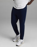 A person wearing a white shirt, Cozy Earth Men’s Recovery Jogger in navy, and white athletic sneakers stands against a plain gray background.|Color:Navy