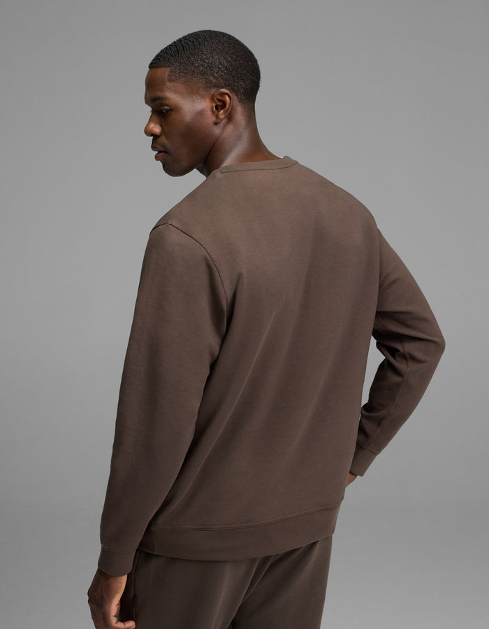 A man stands facing away, wearing the Cozy Earth Men’s StretchTech Crewneck and matching pants against a plain gray background.|Color:Cacao