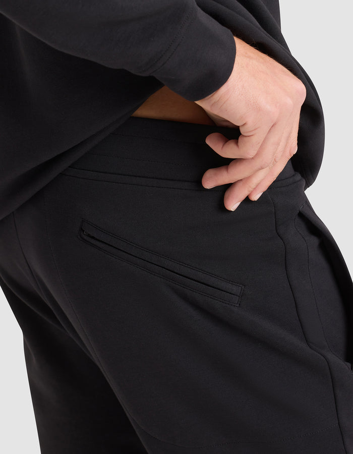 A person wearing the Cozy Earth Men's StretchTech Hoodie & Jogger Set in black rests their hand on the jogger's waistband near the back pocket, with fingers slightly inside. |Color:Jet Black
