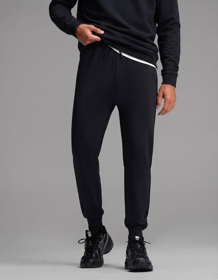 A person is shown standing against a plain gray background wearing the Men's Versa Crewneck & Jogger Set in black by Cozy Earth. Their face is not visible in the image.|Color:Jet Black