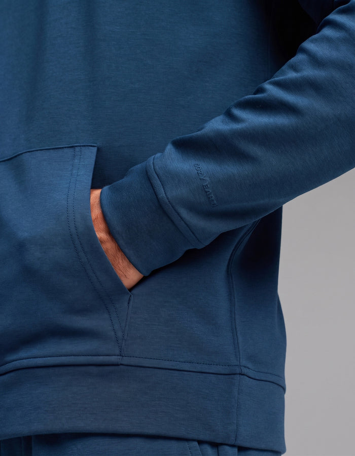 A person wearing the Cozy Earth Men's Versa Hoodie & Jogger Set in blue has their right hand in the front pocket, with the image highlighting the sleeve and pocket details.|Color:Obsidian