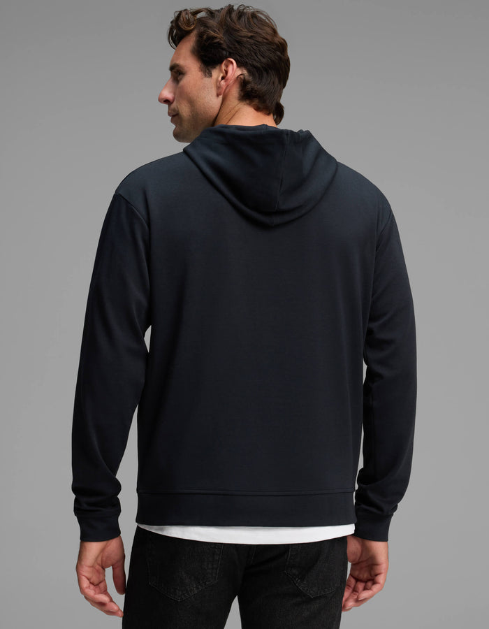 A man stands facing away against a plain gray background, wearing the Cozy Earth Men's Versa Hoodie in black over a white shirt and paired with black jeans.|Color:Jet Black