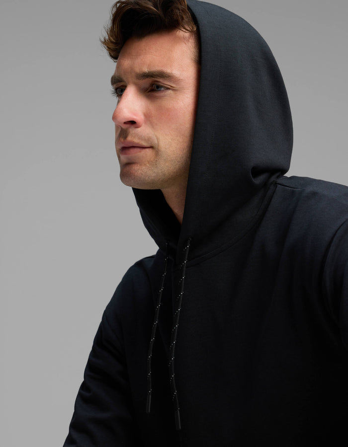 A man wearing the Cozy Earth Men's Versa Hoodie in black looks off to the side against a plain gray background.|Color:Jet Black