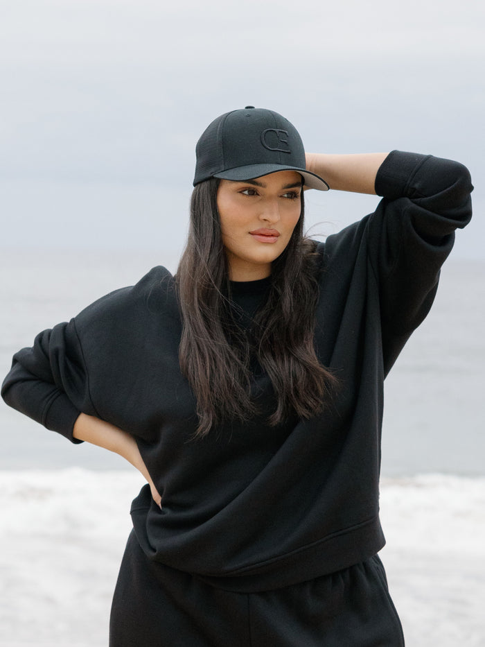 Woman wearing a black cap with a CE logo on a light gray background |Color:Black