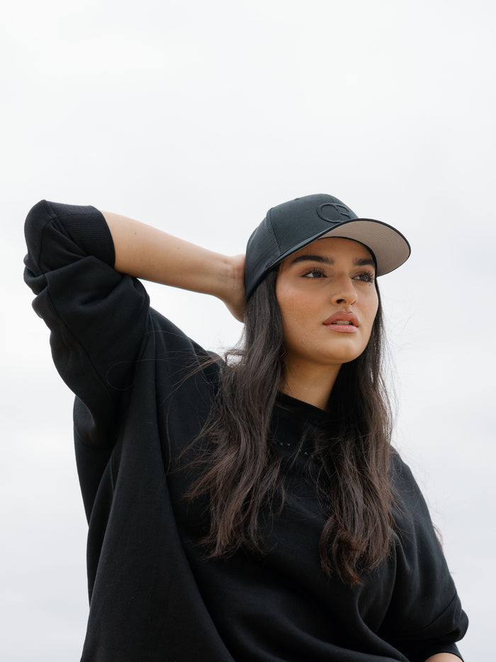 Woman wearing a black cap with a CE logo on a light gray background |Color:Black