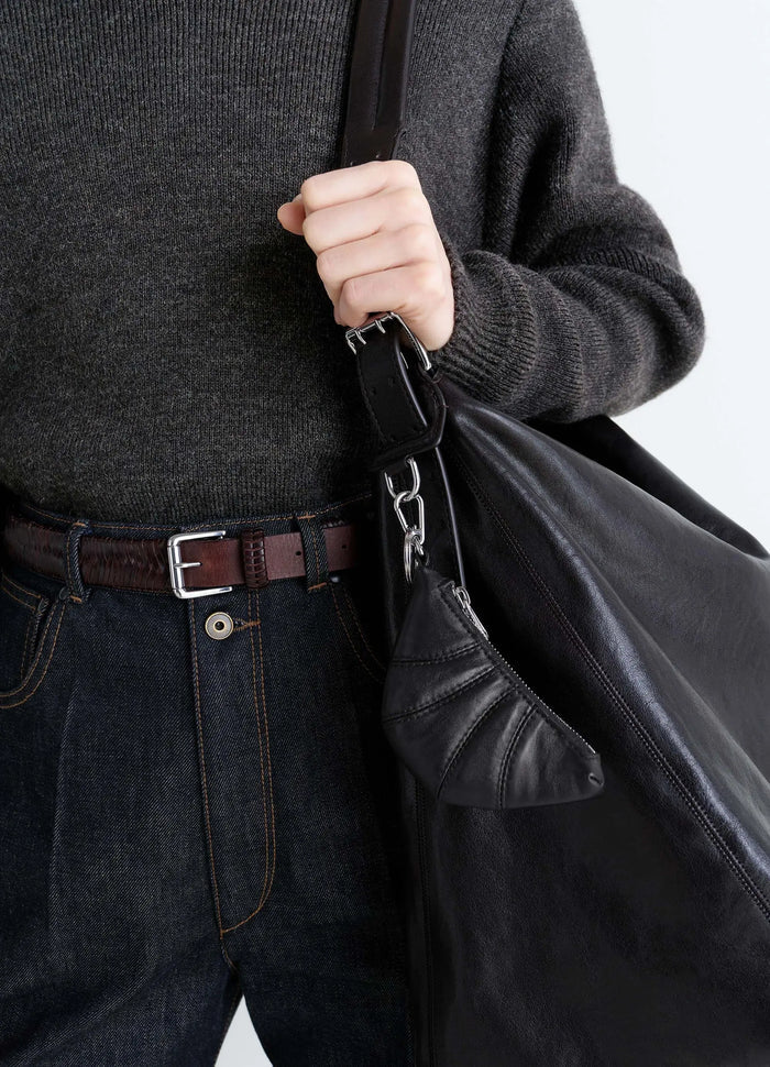 Mini Croissant keyring in black leather by LEMAIRE worn by model holding large leather bag close-up detail