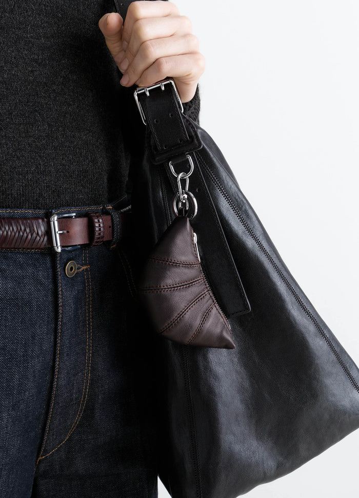 Mini Croissant keyring in brown leather attached to black leather bag worn by model LEMAIRE