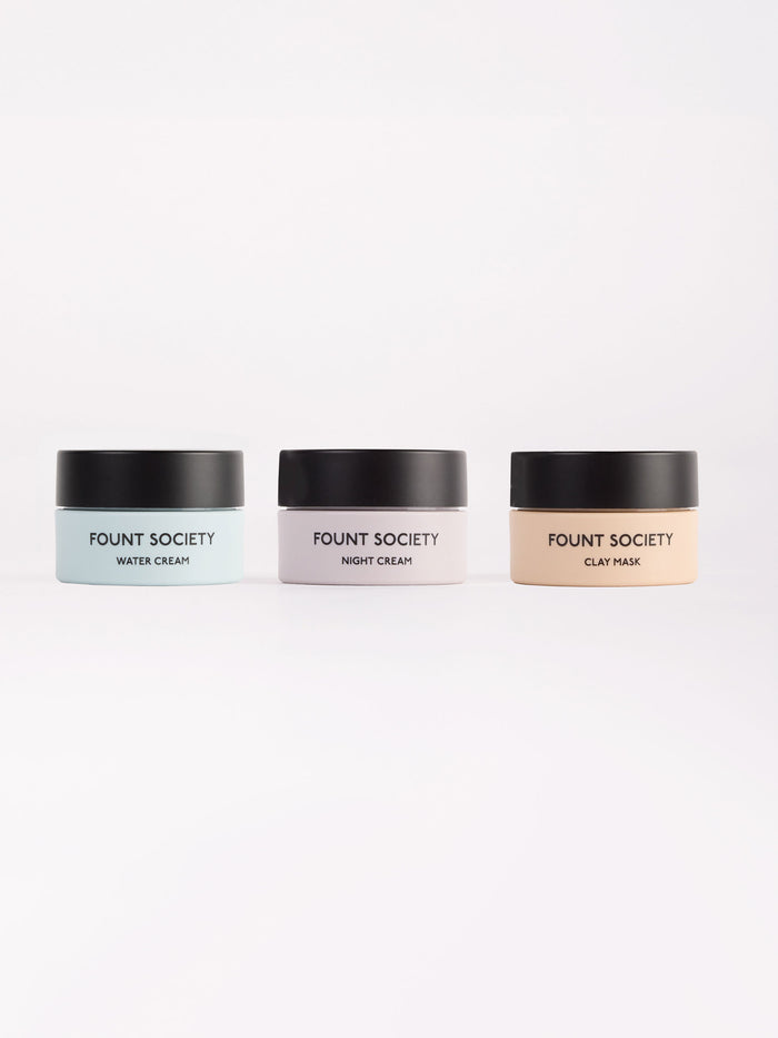 Three containers of the "Mini Moisture Reset Trio" from Cozy Earth are arranged against a white background. From left to right, they include water cream, night cream, and clay mask, each with a black lid and pastel-colored label.