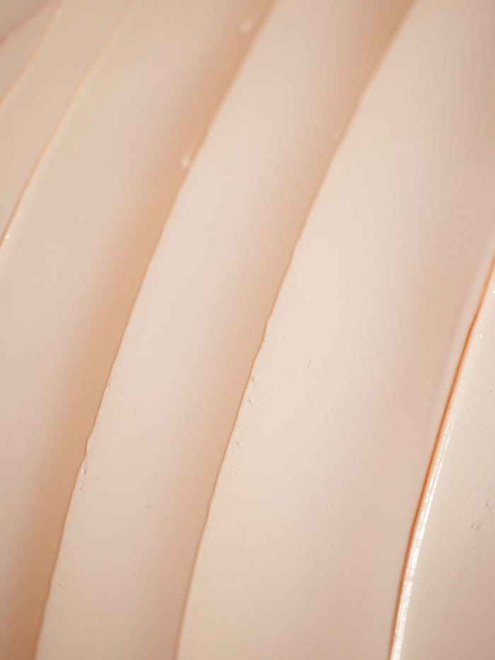 Close-up of Cozy Earth's Clay Mask, showcasing its smooth, curved beige surfaces in parallel lines. The lighting highlights shadows, emphasizing the texture and curvature.
