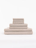The Cozy Earth Nantucket Bath Towel Set features beige textured towels in various sizes, neatly stacked from largest to smallest, set against a plain white background.|Color:Heathered Sand