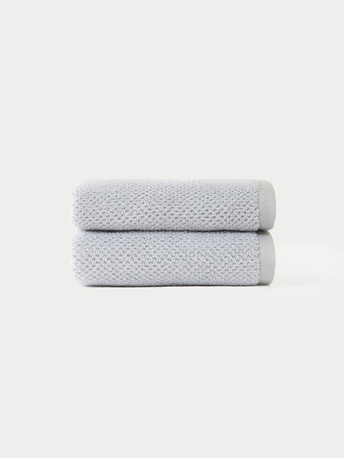 Two Nantucket Bath Towel Set towels by Cozy Earth, neatly folded in light gray and stacked atop each other, displayed against a plain white background.|Color: Heathered Harbor Mist