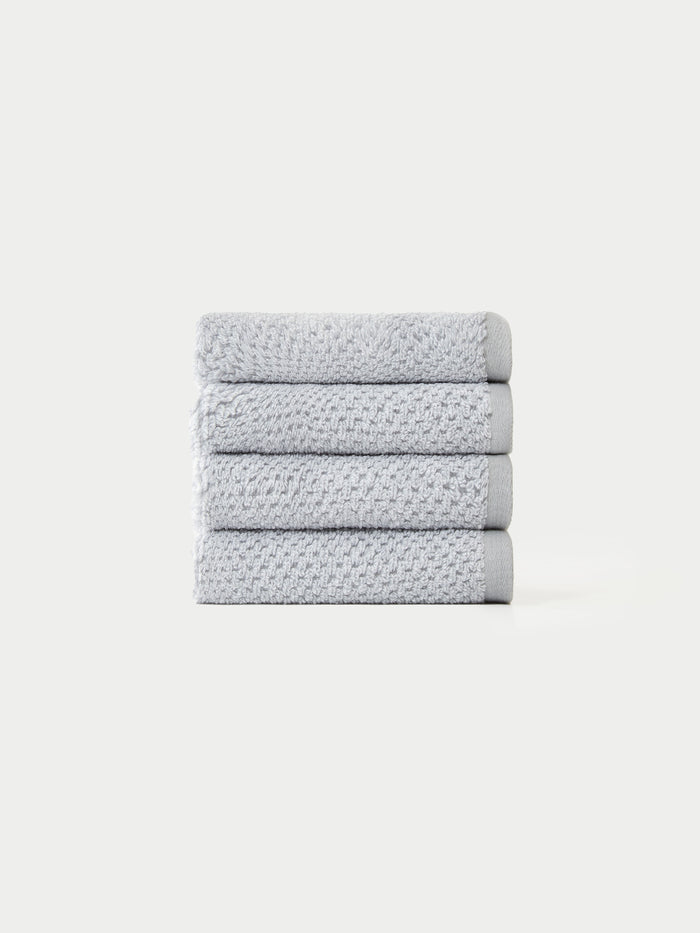 A neatly stacked pile of four light gray, textured towels from the Cozy Earth Nantucket Bath Towel Set on a plain white background.|Color: Heathered Harbor Mist