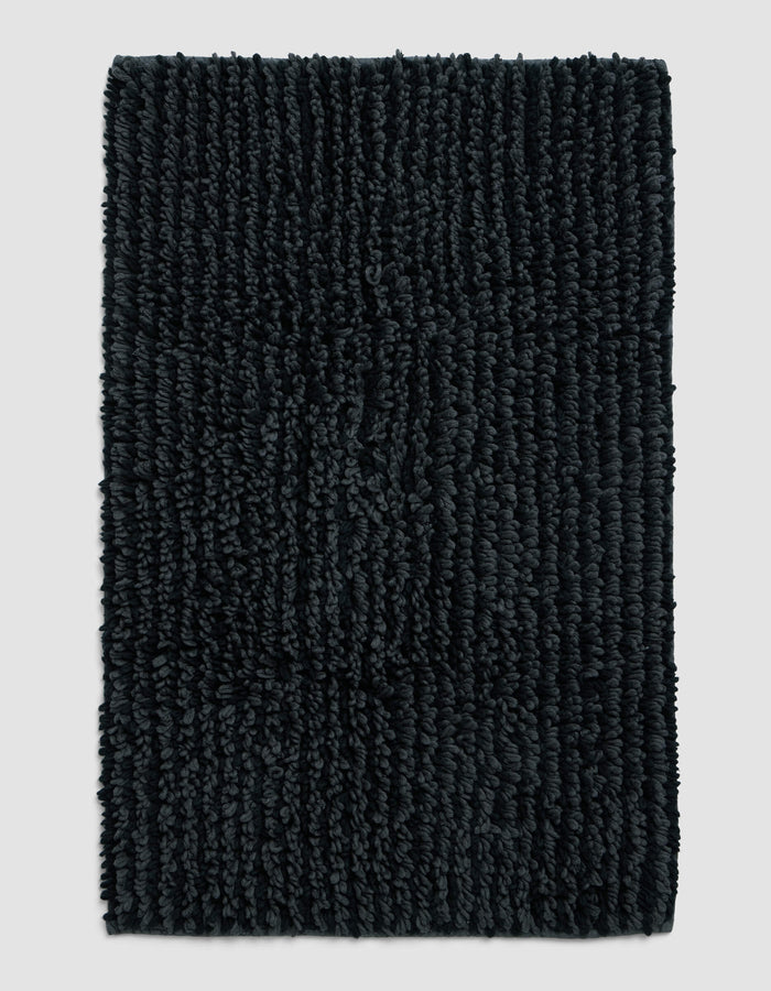 The Cozy Earth Plush Loop Bath Mat, rectangular and dark gray with thick textured fibers, is displayed on a plain light gray background.|Color:Graphite