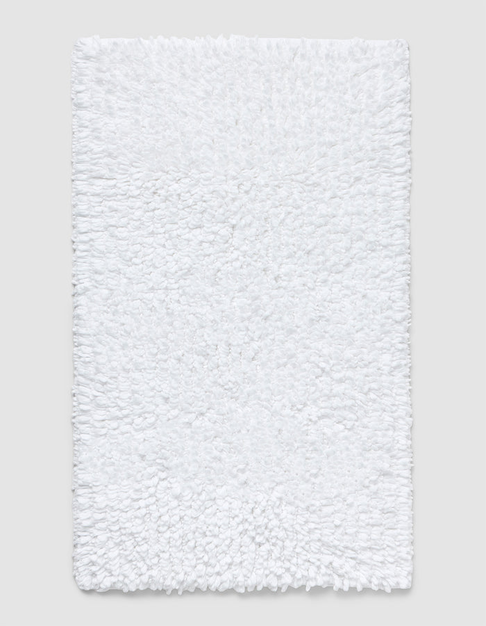 The Cozy Earth Plush Loop Bath Mat is rectangular, white, and features a soft, fluffy chenille shag texture. Shown on a plain light background, it offers plush comfort with its textured surface.|Color:White