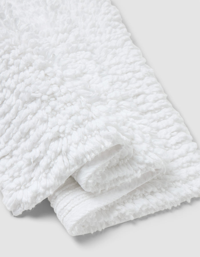 A close-up of the Cozy Earth Plush Loop Bath Mat, folded on a light gray background. The mat’s fluffy, looped texture highlights its softness and absorbency.|Color:White