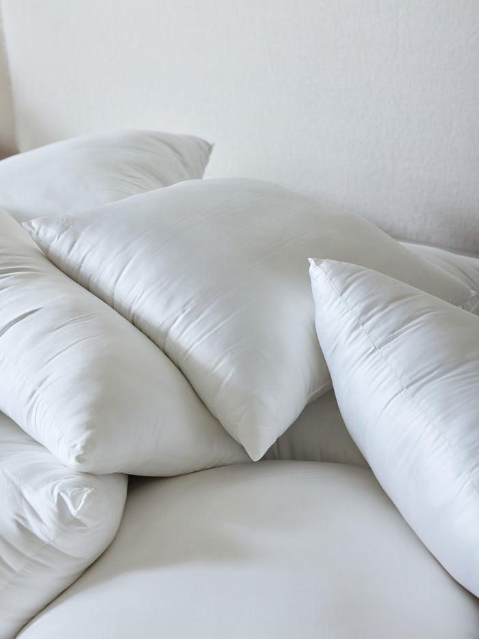 A collection of Cozy Earth Premium Down Alternative Inserts stacked in various orientations. These inserts appear smooth and soft, with a plain white background enhancing their clean and fresh look. |Size:14" x 30"