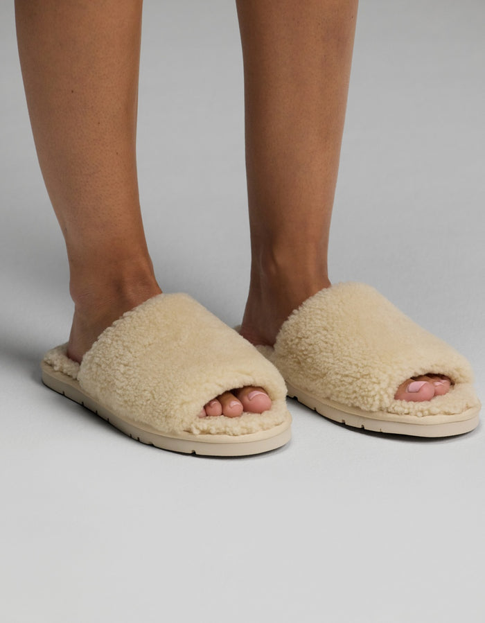 A person wearing Cozy Earth Puffy Sheep Slides stands on a light gray surface.|Color:Natural