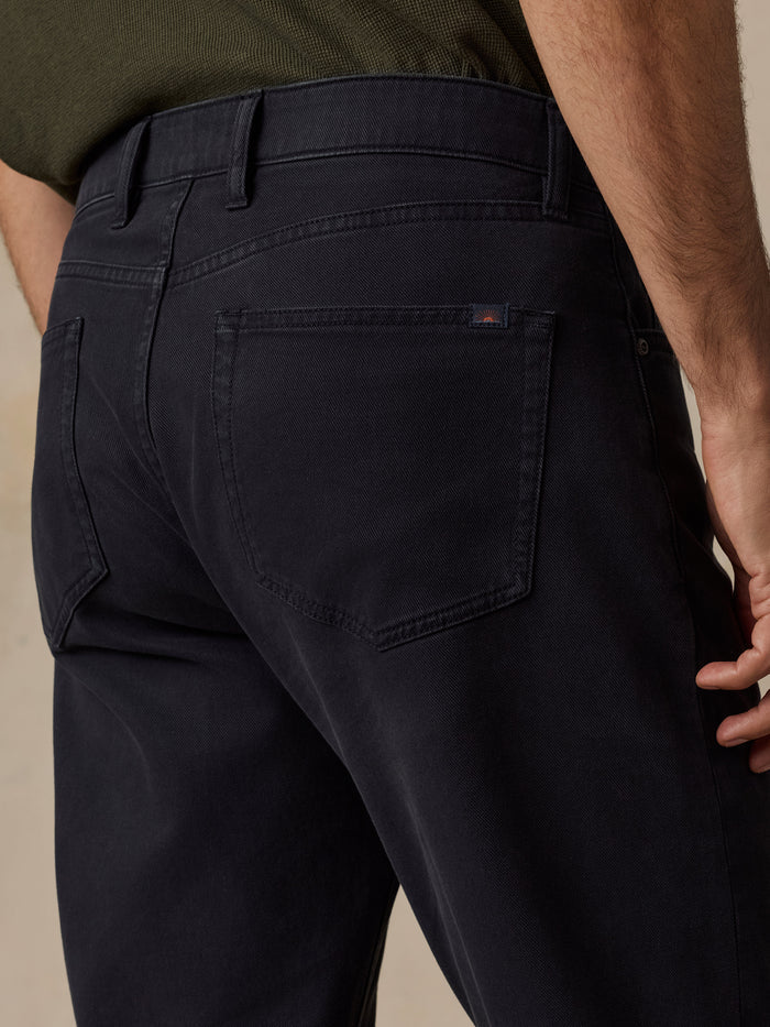 Close-up back view of a person wearing dark navy jeans, showing the waistband, belt loops, back pockets, and a small red Faherty brand tab on the pocket.