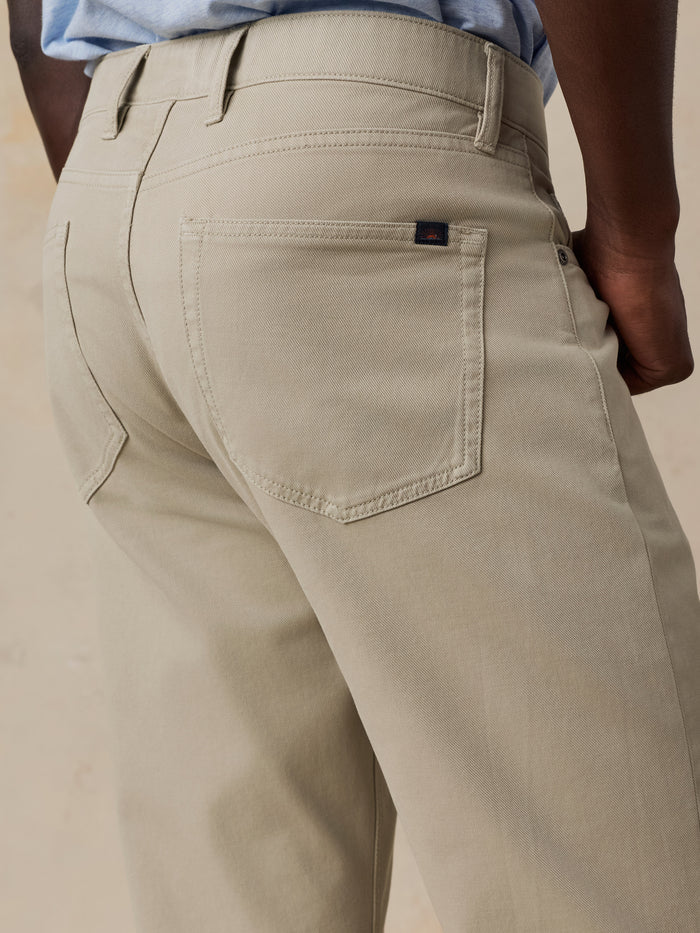 Close-up back view of a person wearing light beige chinos or casual trousers, showing the back pocket, belt loops, waistband, and part of the blue shirt at the waist.