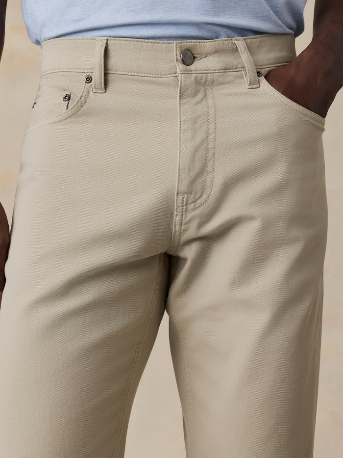 Close-up of a person wearing light beige chino pants with a light blue shirt partially visible at the top, against a soft beige background.