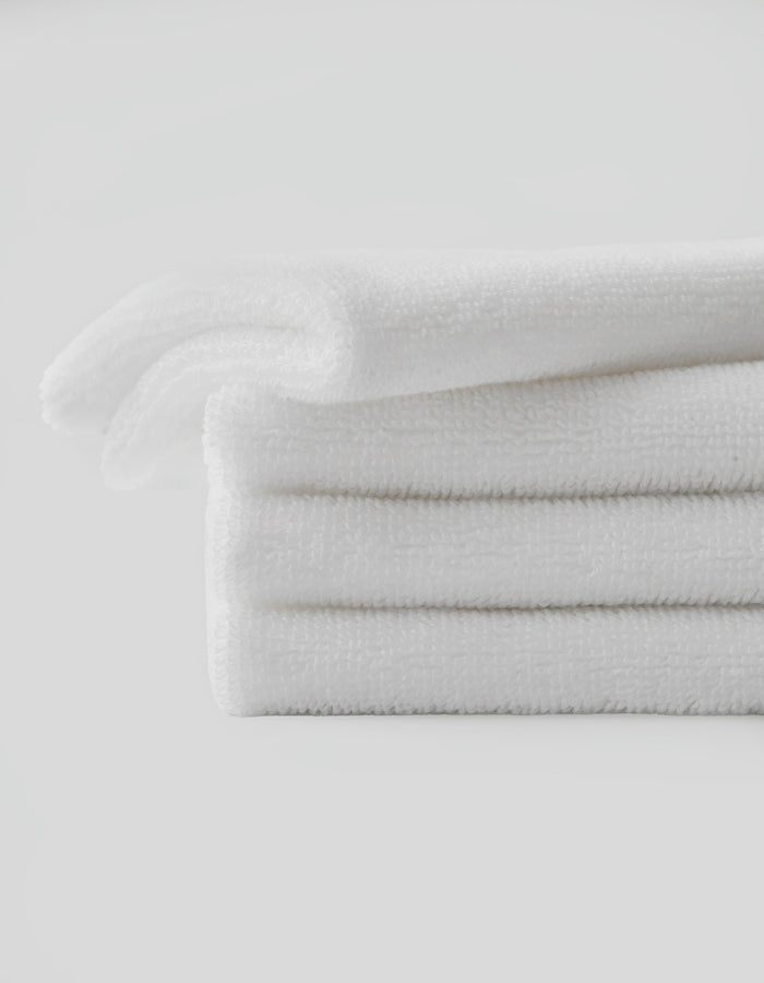 A neatly folded stack of three white towels from Cozy Earth's Revitalizing Pair set is placed against a plain white background. The towels appear soft and fluffy, with a clean, fresh look. The arrangement emphasizes their texture and pristine condition.
