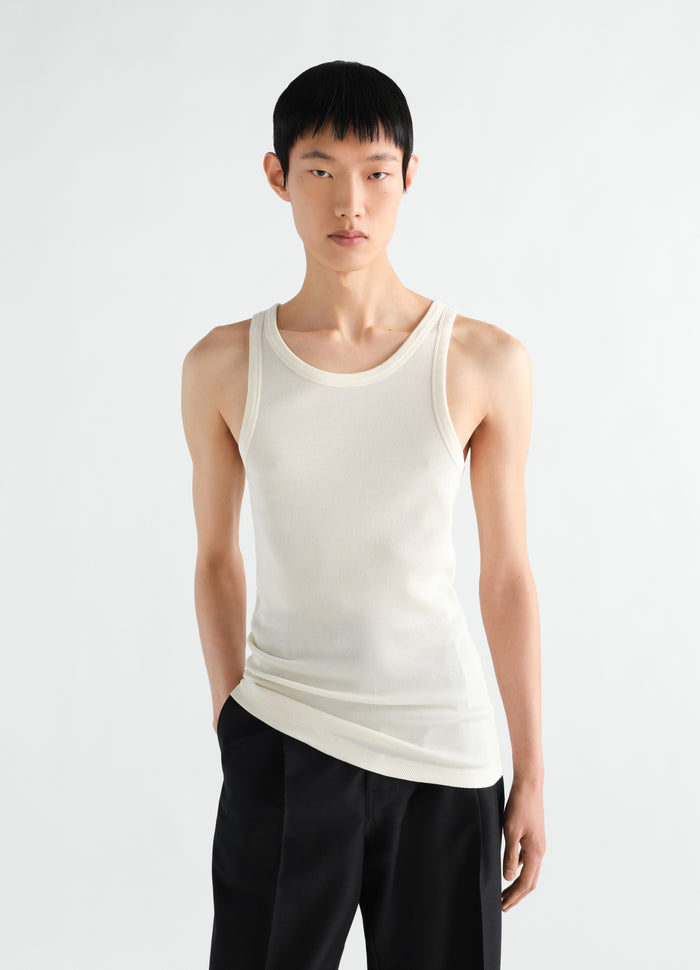 Tank top in off-white ribbed jersey by LEMAIRE worn by model front view with black pants and white background