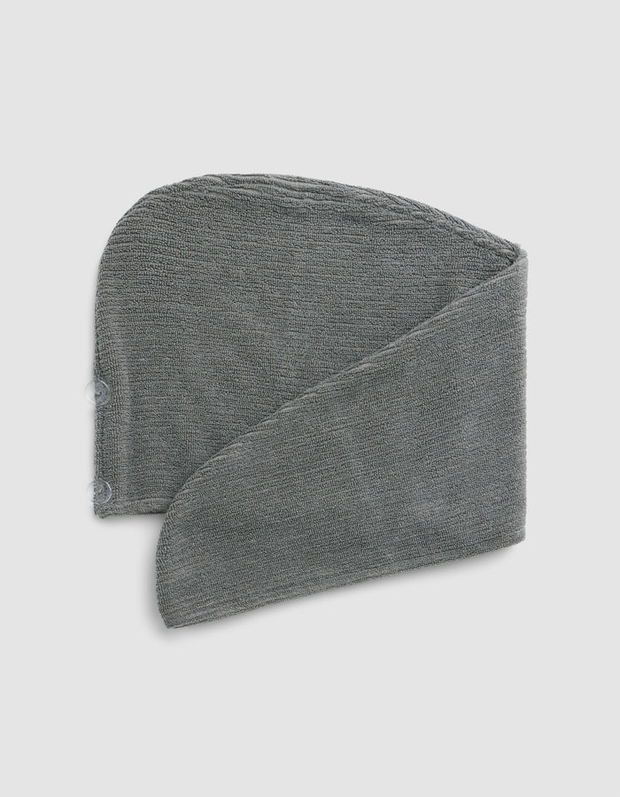 The Cozy Earth Ribbed Terry Hair Towel in grey is pictured folded in a spiral shape against a light grey background.|Color:Charcoal