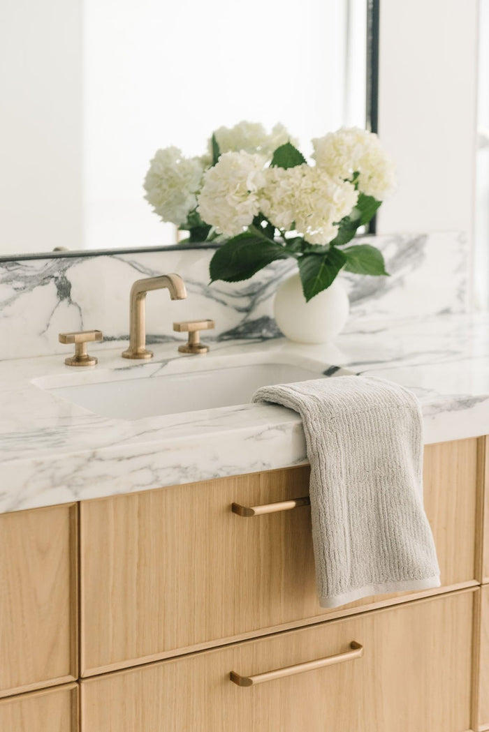 Ribbed Terry Hand Towels in the color Light Grey. Photo of product taken with the product draped over a white marble sink. |Color:Light Grey