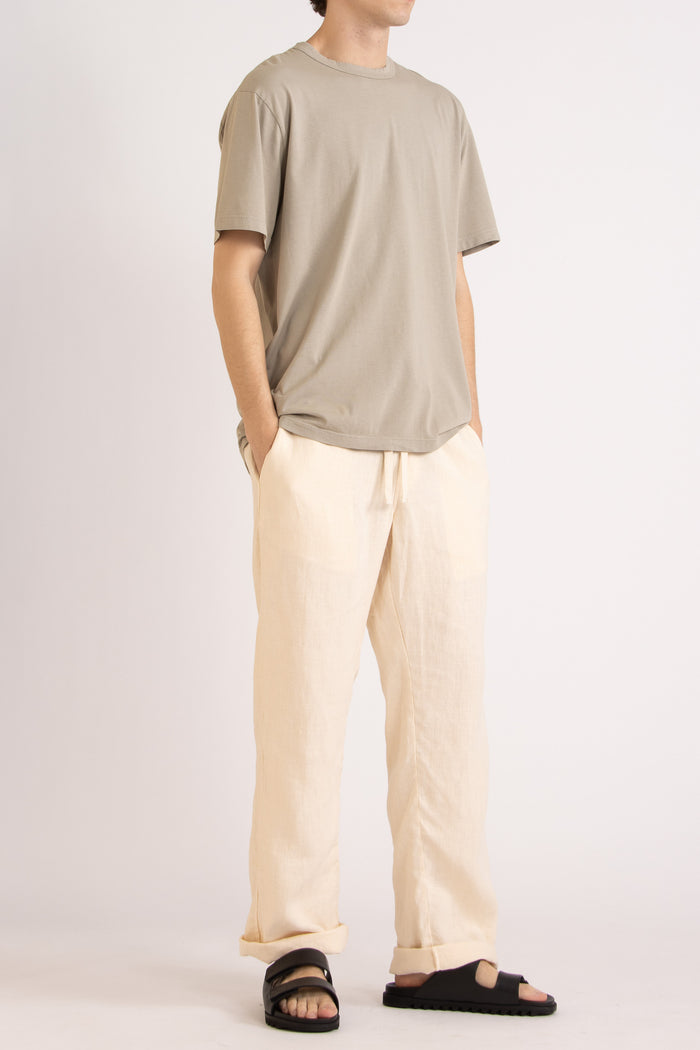 model wearing a oat cotton t-shirt and natural linen pants on a plain background, front side view