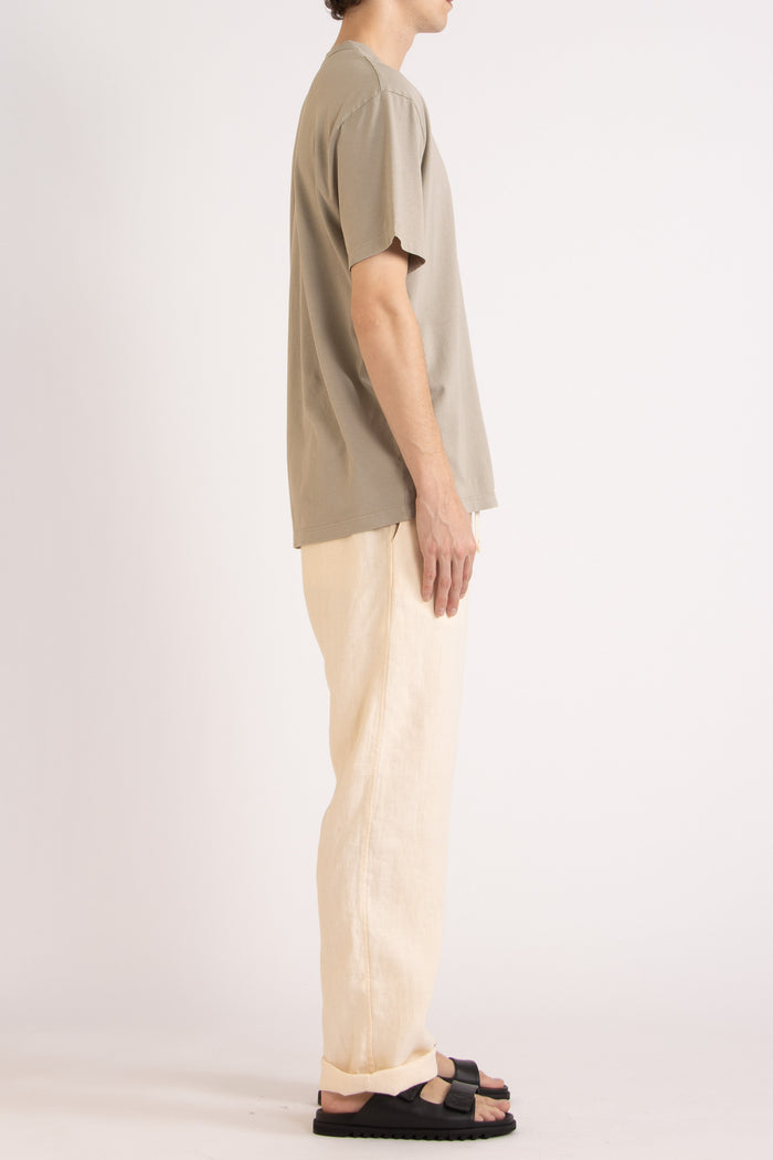 model wearing a oat cotton t-shirt and natural linen pants on a plain background, side view