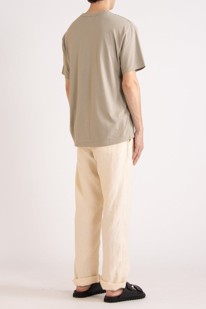 model wearing a oat cotton t-shirt and natural linen pants on a plain background, side back view