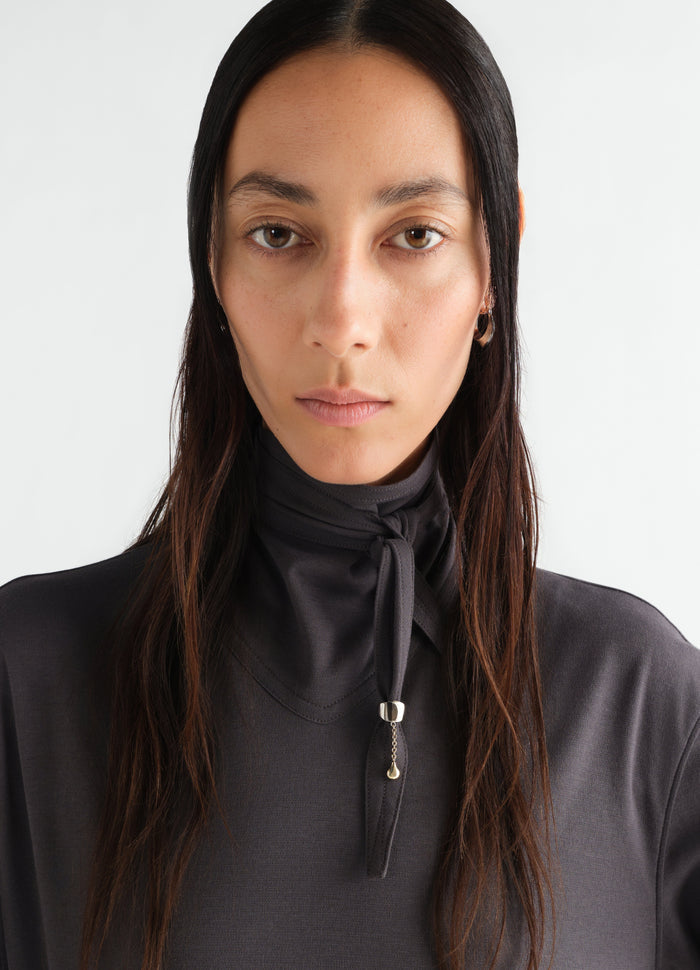 Scarf ornament in brass by LEMAIRE worn by model with tied dark grey fabric detail close-up front view